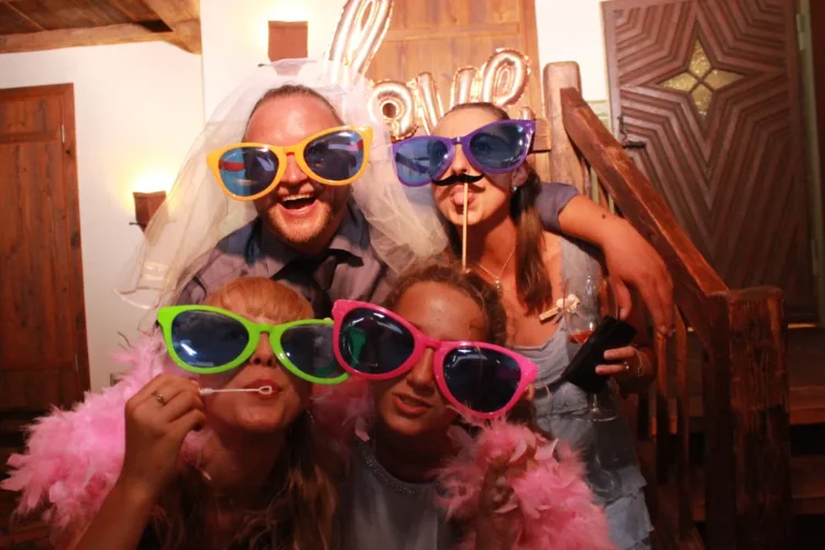 Hochzeitsgäste posieren mit großen Brillen und lustigen Requisiten in der Fotobox bei einer Hochzeit in Bayern