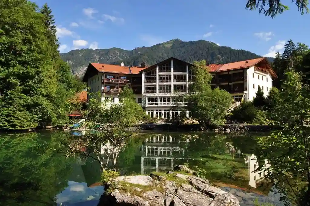 Hotel am Badersee mit Blick auf den klaren See, umgeben von Wald und Bergen bei hellem Tageslicht.