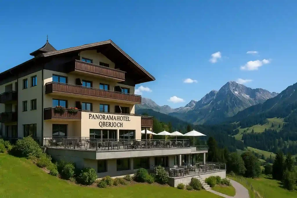 Panoramahotel Oberjoch von außen, mit großer Sonnenterrasse und Blick auf die Allgäuer Alpen bei klarem, sonnigem Himmel.